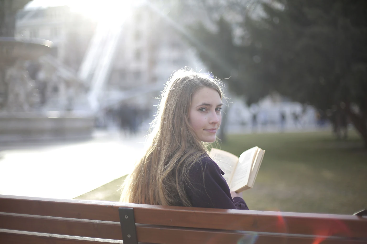 Mulher com um livro em um banco de parque, iluminada pelo sol.